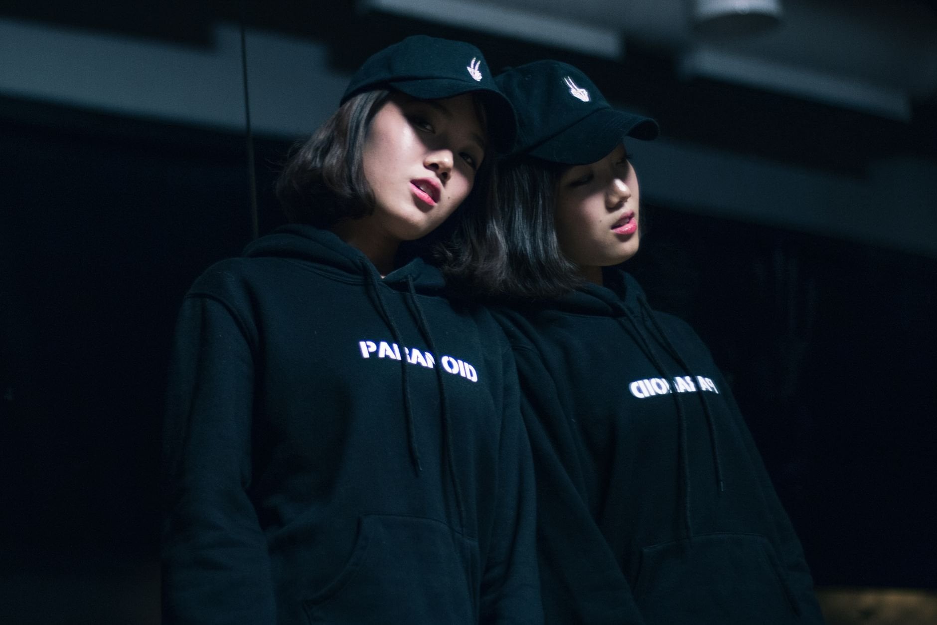 A fashionable woman in a dark moody setting wearing streetwear hoodie and cap