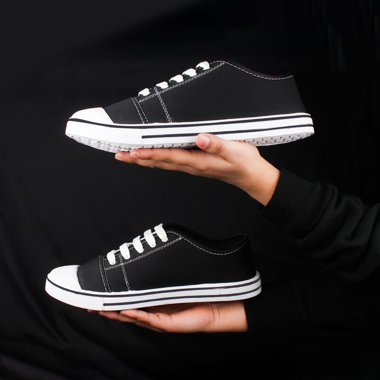 Black sneakers held against a dark background